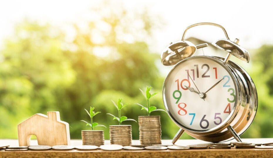 Un reloj y un montón de monedas que simbolizan los beneficios de ahorrar dinero durante el tiempo.